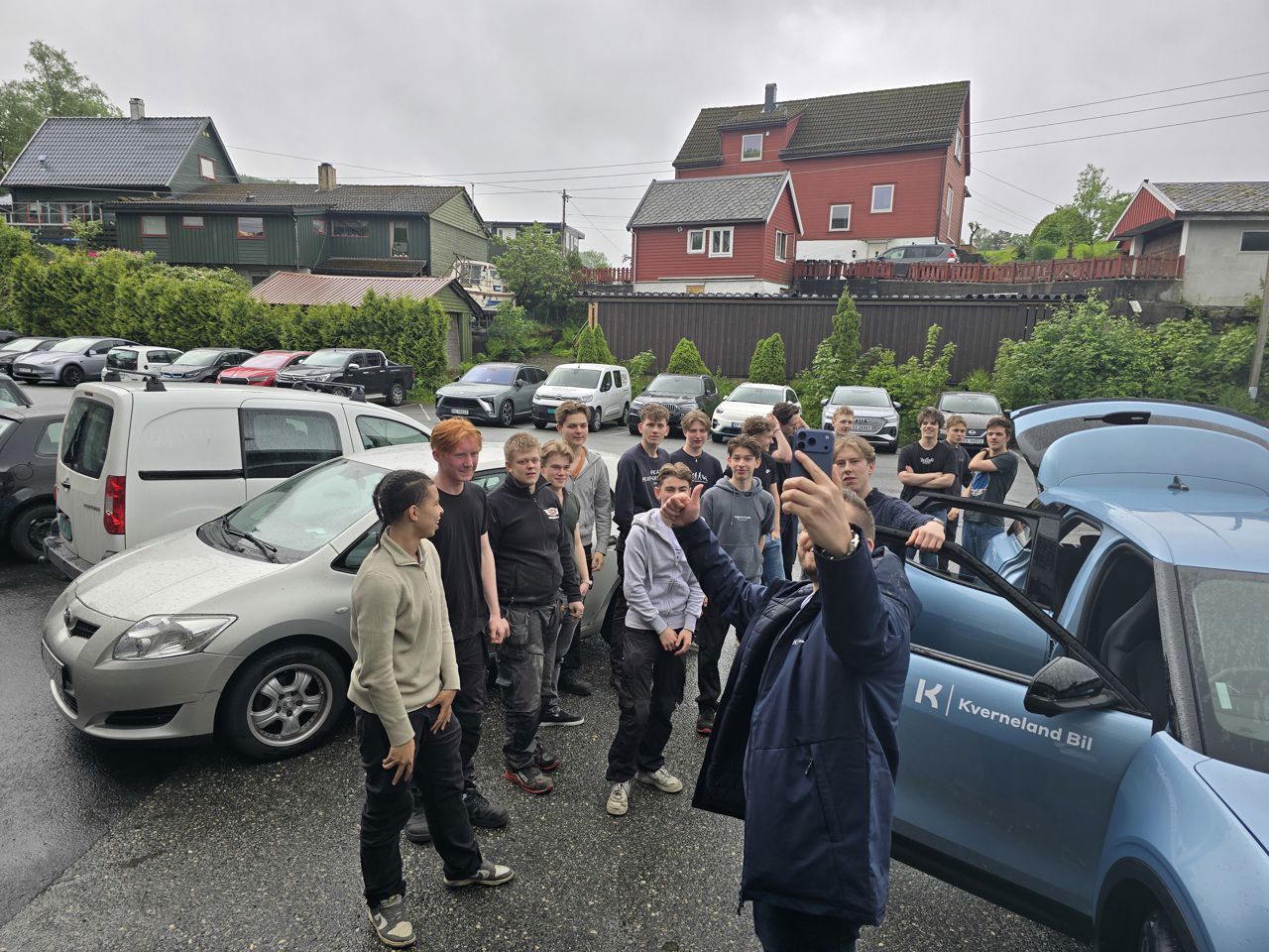 Ein mann tar ein selfie saman med ei klynge elevar og den blå Forden på plassen utanfor skulen.