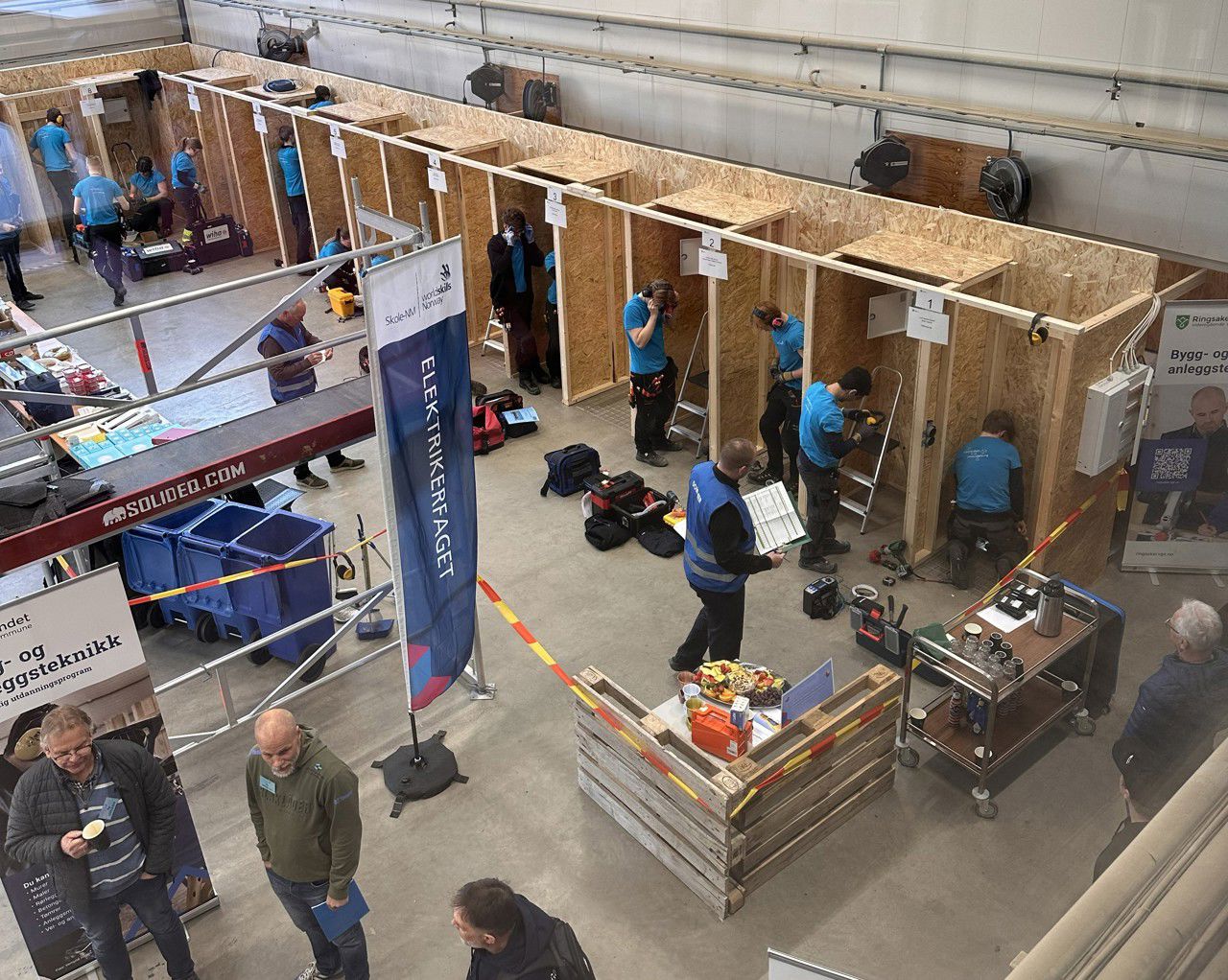 Konkurranselokalet i elektrofaget, sett i fugleperspektiv. Dei ulike laga jobbar i kvart sitt avgrensa område. To dommarar og nokre tilskodarar følgere med.