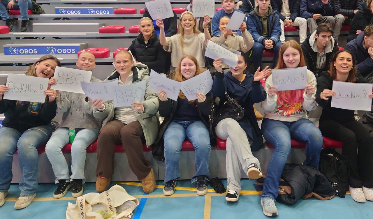 Heiagjeng på tribunen - ei gruppe elevar held opp ark med namna til spelarane på 4PBYb-laget