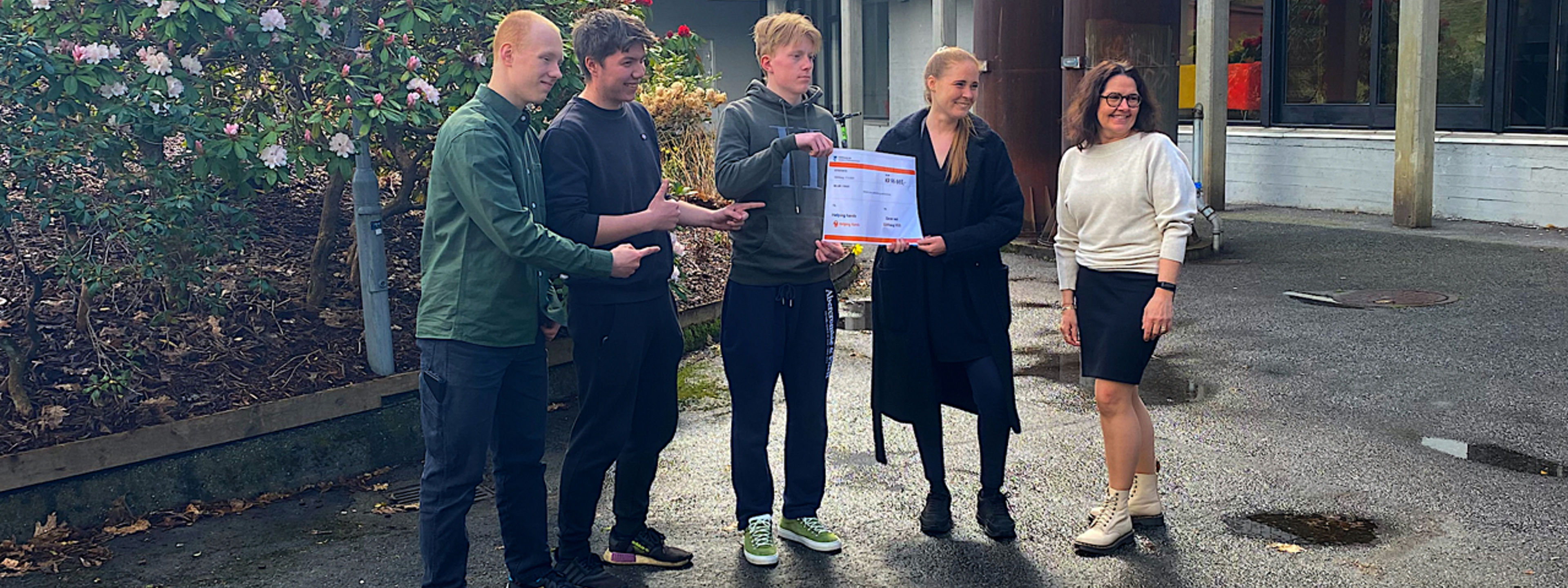 Daniélla held den store sjekken saman med ein representant frå elevrådet, mens rektor og to andre elevar ser på.