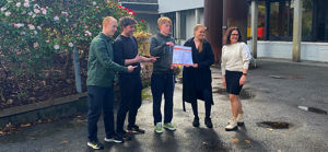 Daniélla held den store sjekken saman med ein representant frå elevrådet, mens rektor og to andre elevar ser på.