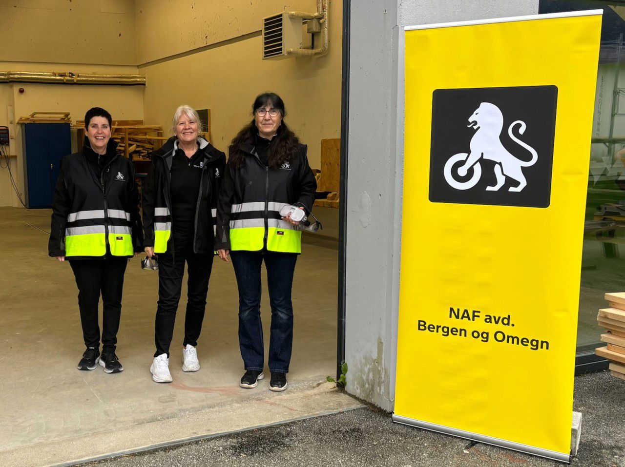 Tre representantar frå NAF avd. Bergen og omegn står oppstilte ved sida av eit NAF-banner.