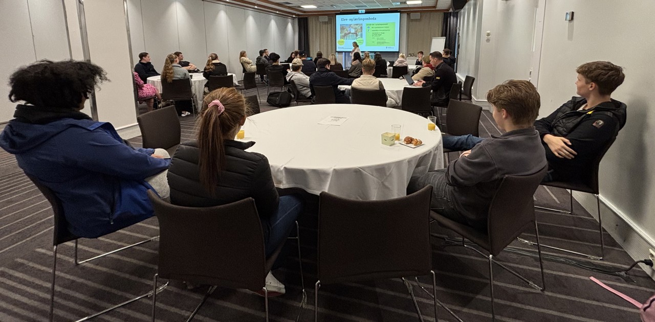 Ei gruppe elevar (tillitsvalde) samla ved fleire runde konferansebord følger med på presentasjonen til elev- og lærlingomboda