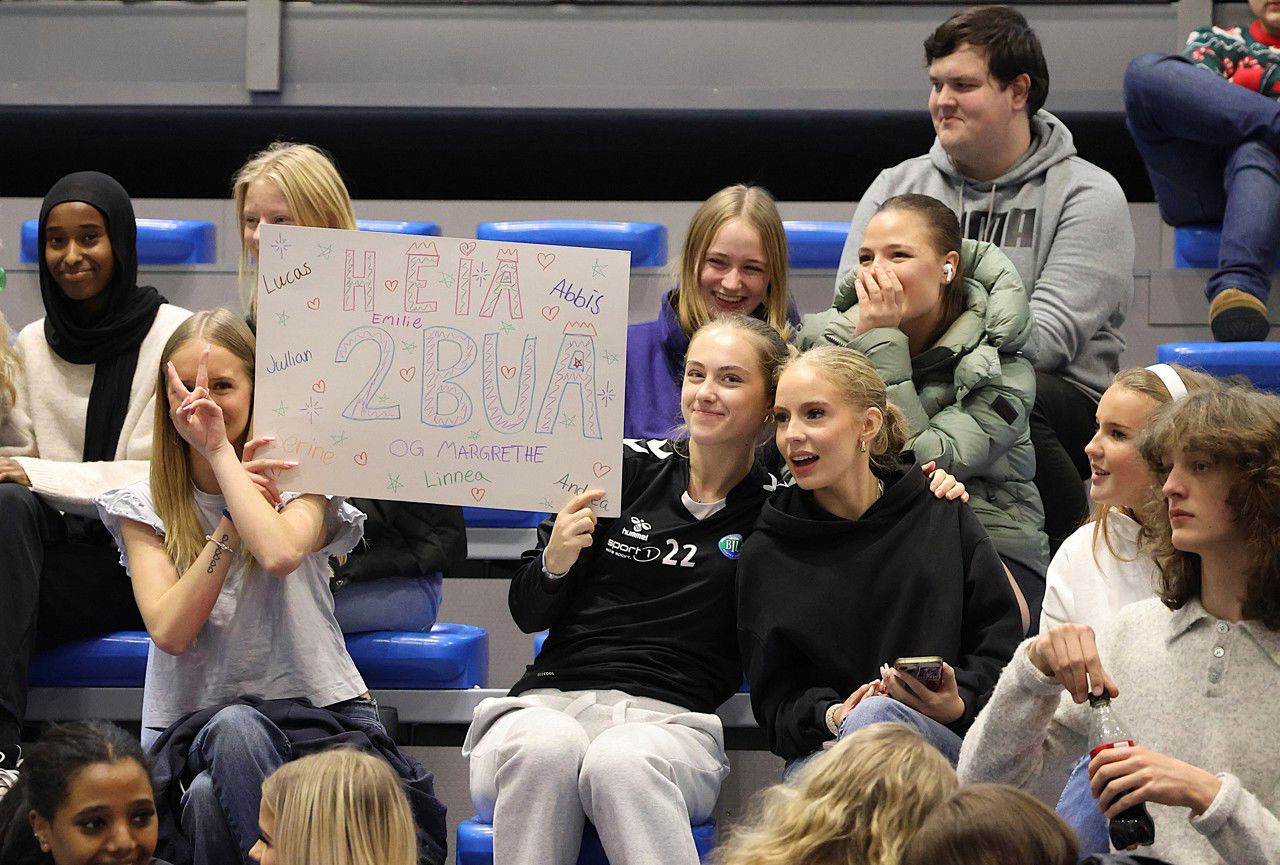 Ei gruppe elevar på tribunen heiar på laget sitt mens dei held opp ein plakat med slagord