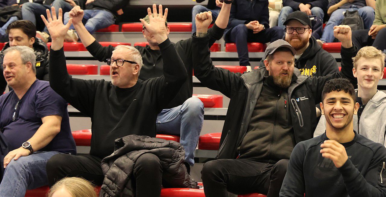 Nokre lærarar og elevar på tribunen. Lærarane løftar armane over hovudet i begeistring (på ordre...)