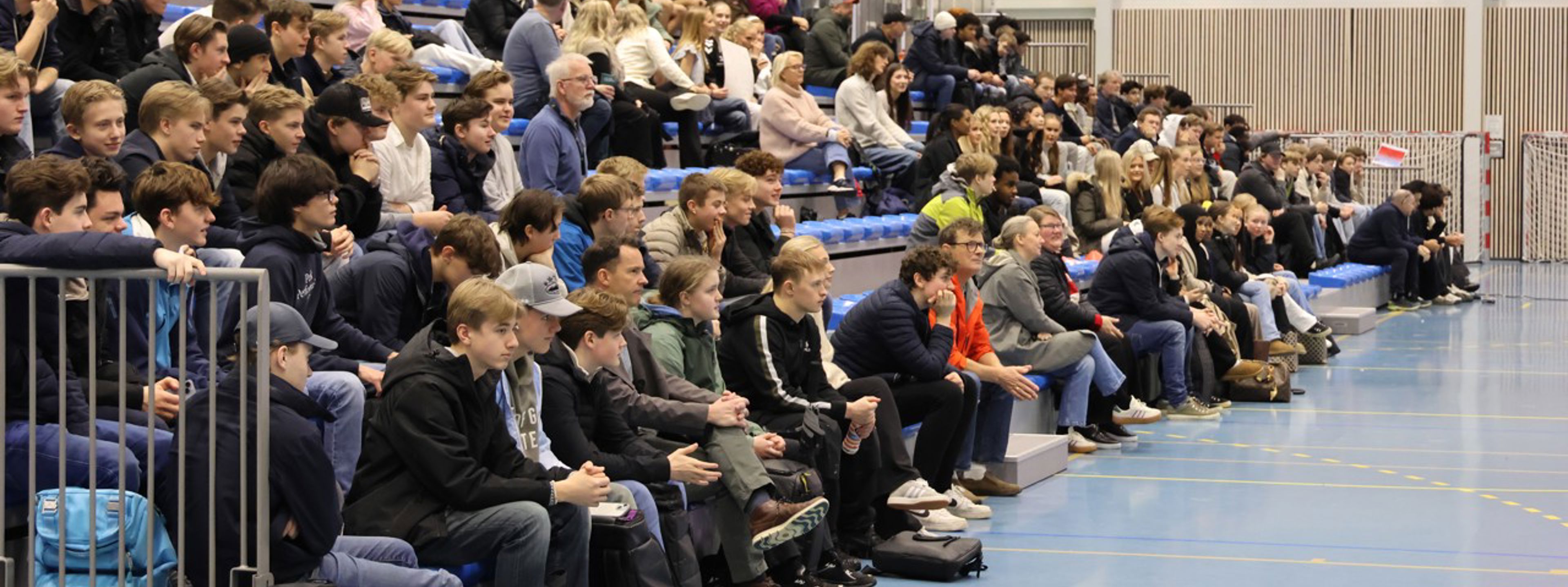 Tribune langs eine veggen i Fana Arena, full av elevar og lærarar.