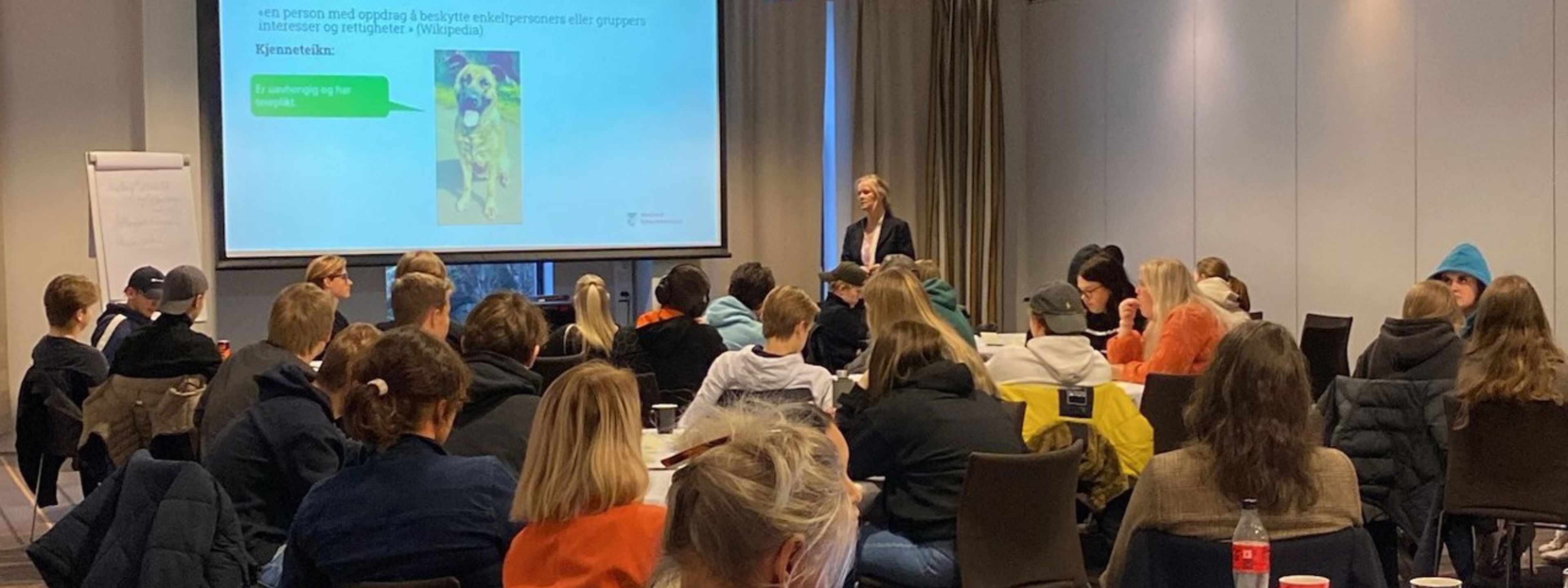 Elev- og lærlingombodet i Vlfk viser ein presentasjon om arbeidet sitt foran eit rom fullt av klassetillitsvalde og eit utval av tilsette.